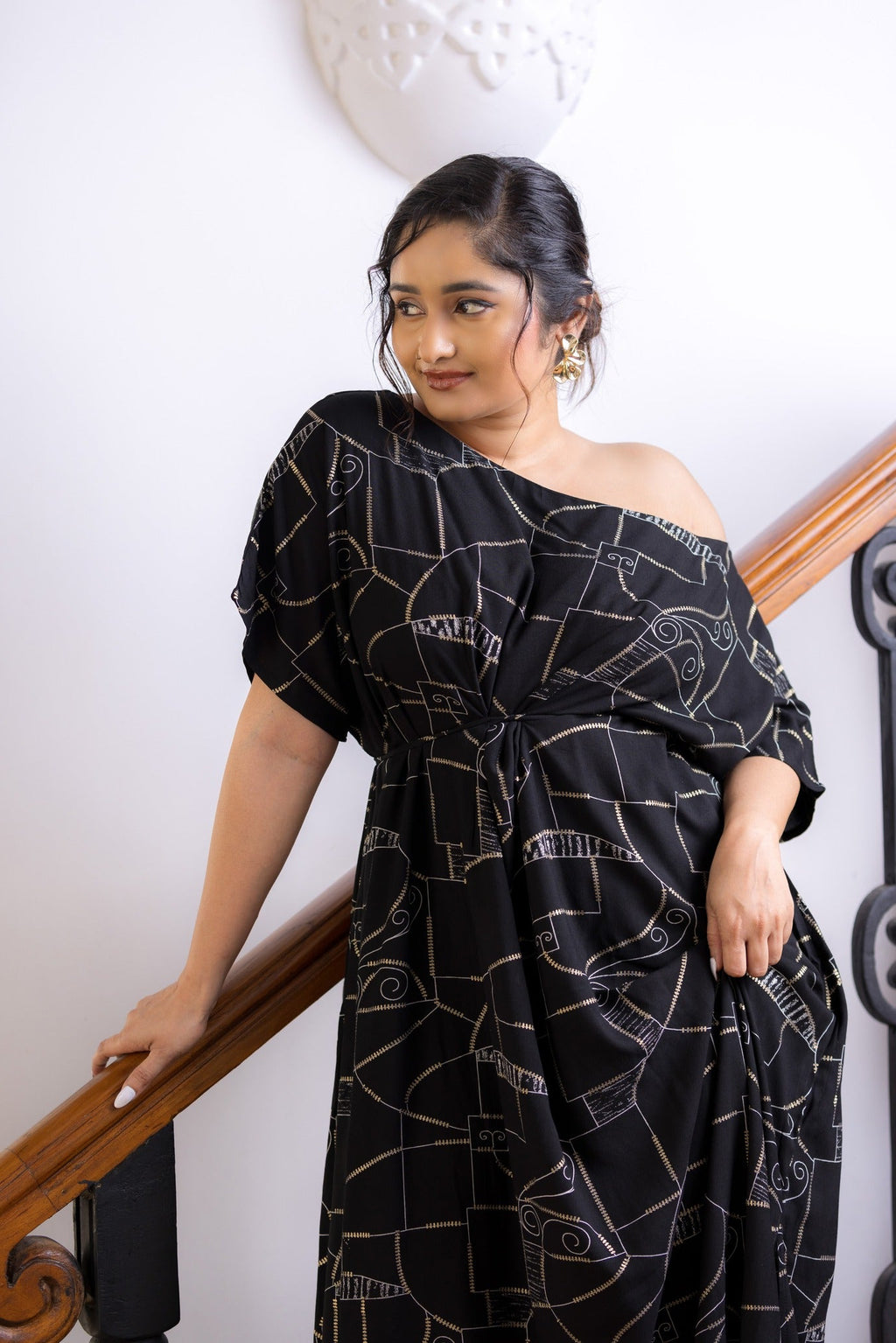 Woman wearing a black off-shoulder dress with white patterns, standing indoors.