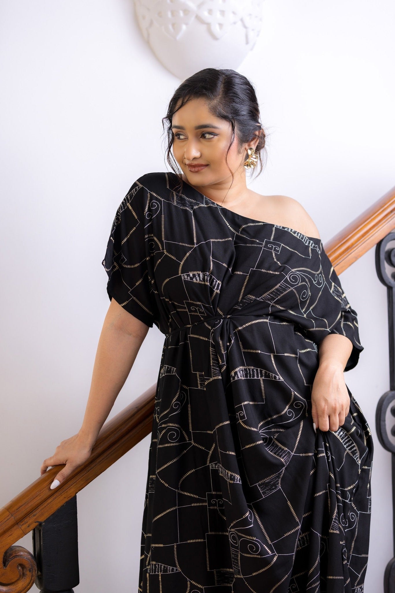 Woman wearing a black off-shoulder dress with white patterns, standing indoors.